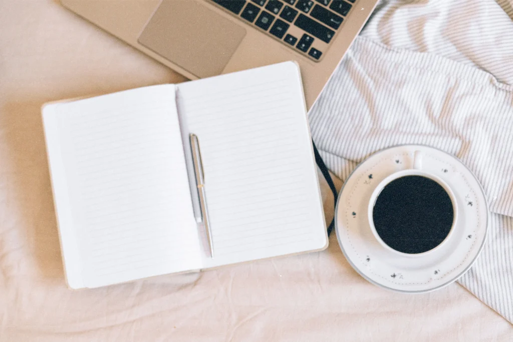 Quaderno aperto con penna e tazza di caffè accanto a un laptop, scrivania minimal per chi vuole aprire un blog sul sito