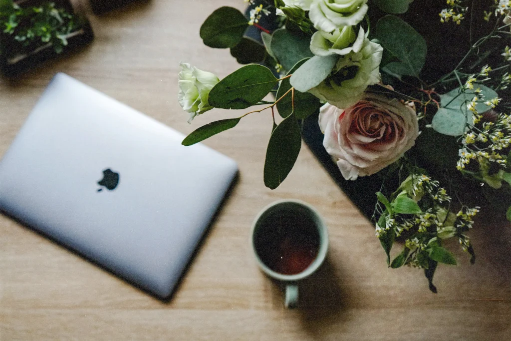 Closed laptop, tea and flowers on light wood desk, homepage checklist